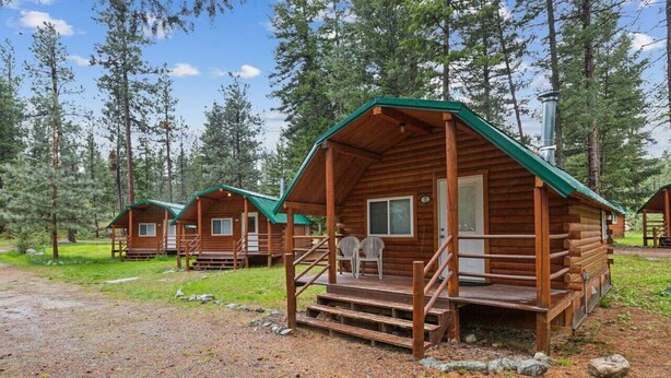 A row of log cabins with green roofs, wooden decks, and a clear view of the surrounding forest.