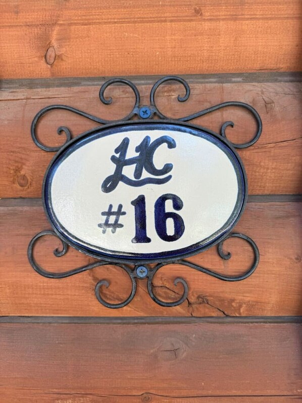 A house number sign with the number 16, mounted on a wooden wall.