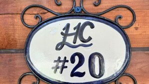 Un panneau indiquant le numéro de maison, avec les lettres « HC » et le chiffre « 20 », le tout sur un fond en bois.