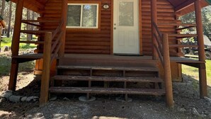 Una cabaña de madera con un porche, una puerta principal y una ventana pequeña.