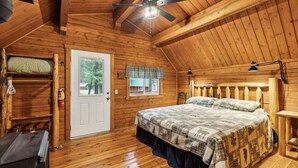 A cozy cabin room with a wooden ceiling, a bed with a plaid bedspread, a window with a plaid valance, and a door with a white frame. - Log Cabin Retreat in the Montana Wilderness (Hamilton)
