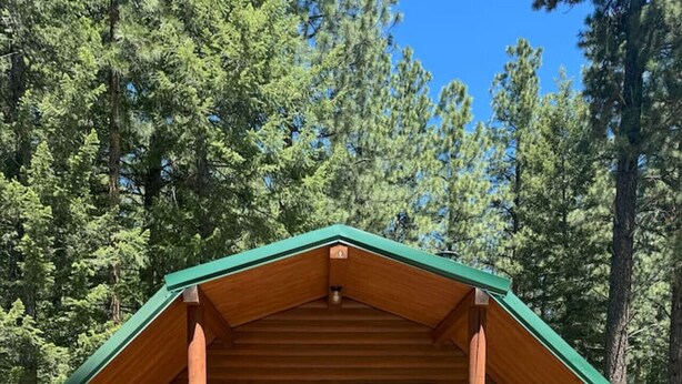 A small wooden cabin with a green roof, a front door, and a porch with steps leading up to it. - Log Cabin Retreat in the Montana Wilderness (Hamilton)