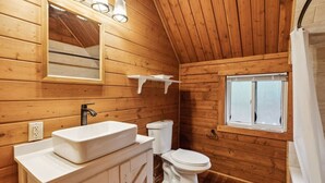 A wooden cabin bathroom with a white sink, toilet, and a window. - Log Cabin Retreat in the Montana Wilderness (Hamilton)