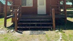 Una cabaña de madera con un porche, una puerta principal y un ventanal pequeño.