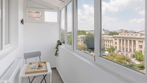 A balcony with a view of a university building, a chair, a table with a tray, and a potted plant. - Playful & Bright 1BR near The Faculty of Law (Bucharest)