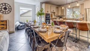 Une cuisine moderne avec un coin repas, comprenant une longue table en bois, des tabourets de bar et une grande horloge murale.