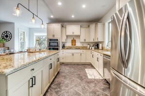 A modern kitchen with granite countertops, stainless steel appliances, and light-colored cabinetry. - Sleeps 18, Hot Tub, Arcade, 3 Living Areas (Redmond)