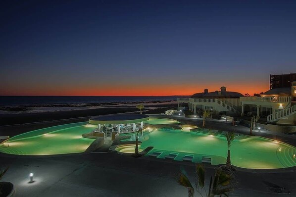A resort pool area with a view of the ocean at sunset.