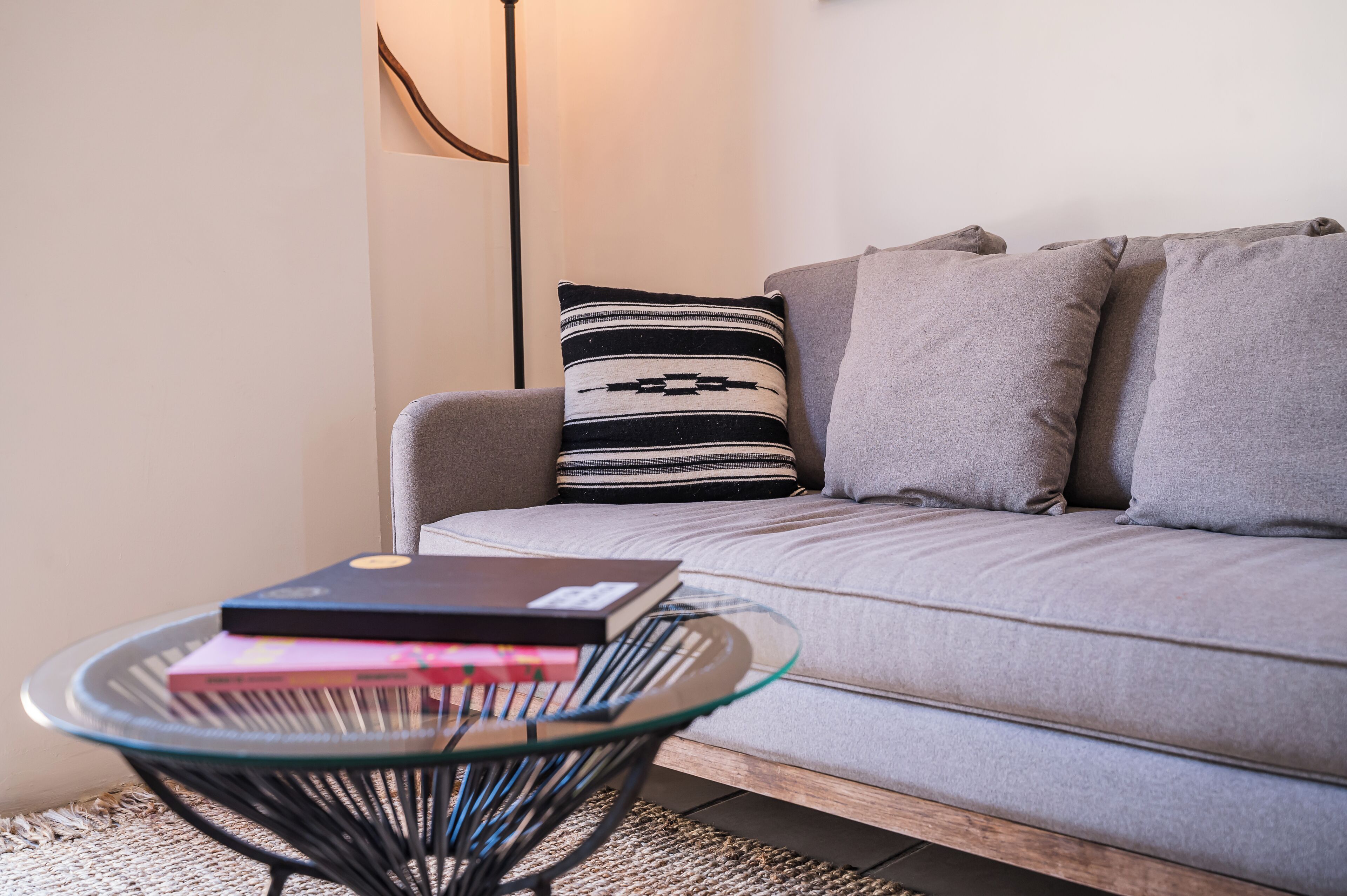 Een moderne woonkamer met een grijze bank, een glazen bijzettafeltje met boeken en een kussen met een patroon.