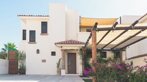 A modern two-story building with a beige facade, a brown door, and a covered patio area with a wooden pergola. - Grand Villa w Private Patio & Parking  (San José del Cabo)