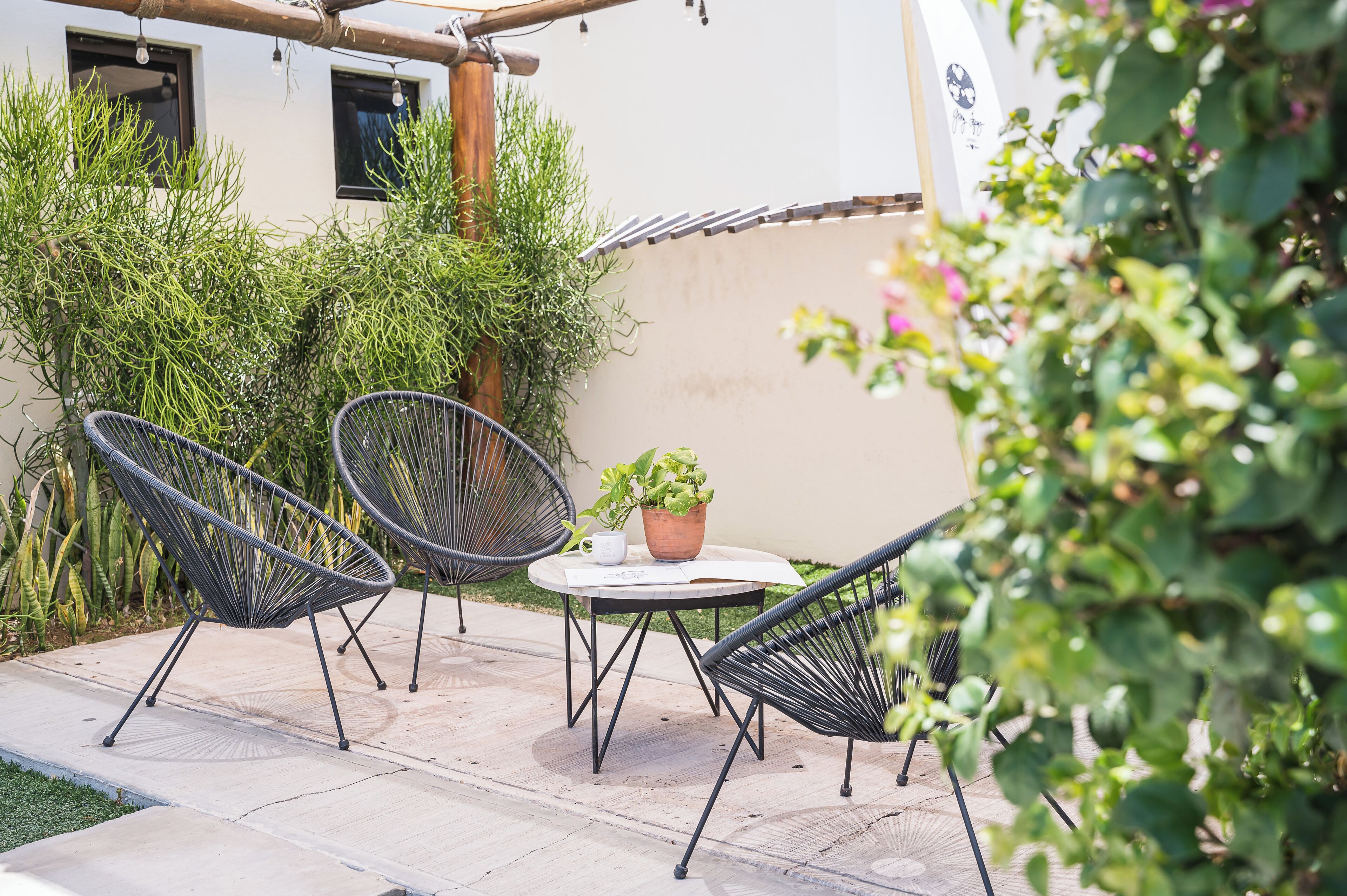 Eine Terrasse im Freien mit zwei schwarzen Stuhlen aus Draht, einem kleinen runden Tisch und einem Blumentopf.