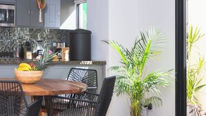 A modern kitchen with a dining area, featuring a wooden table, black wicker chairs, and potted plants. - Grand Villa w Private Patio & Parking  (San José del Cabo)