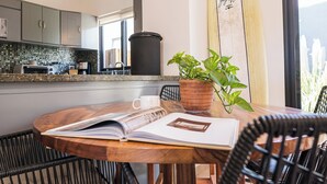 A modern kitchen with grey cabinets, a black trash bin, a wooden table with a book, a white mug, and a potted plant. - Grand Villa w Private Patio & Parking  (San José del Cabo)