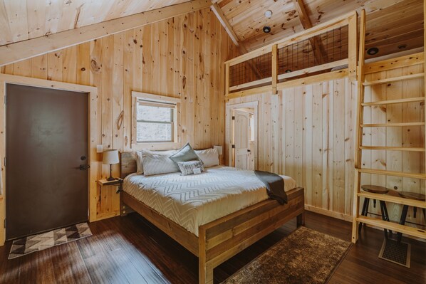 Ein Zimmer aus Holz mit Bett, Fenster, Tür und Ablagefläche.