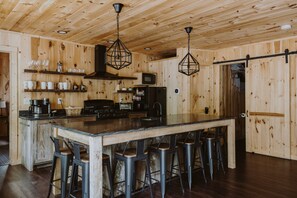 A wooden interior with a central island, bar stools, a microwave, and a stove.