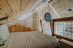 Une pièce de cabane en bois comprenant un lit, une décoration murale circulaire et une fenêtre à carreaux.