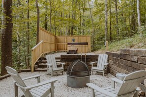 Eine Holzterrasse mit eingebauter Feuerstelle und Sitzgelegenheiten, umgeben von Bäumen.