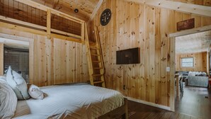 Interieur van een houten hutje met een bed, een ladder, een televisie en een bordje dat een staatspark aangeeft.