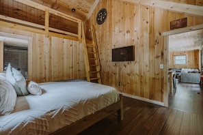Innenansicht einer Holzhütte mit einem Bett, einer Leiter, einem Fernseher und einem Schild, das einen Staatspark kennzeichnet.