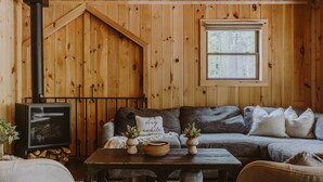 Ein gemütliches Blockhauss-Interieur mit einer Holzwand, einer Couch, einem Tisch mit Dekoration und einem Kamin.