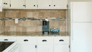 A kitchen with white cabinets, a granite countertop, a coffee maker, and a refrigerator.