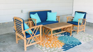 A wooden outdoor seating area with a blue sofa and matching chairs, a small table, and a patterned rug.