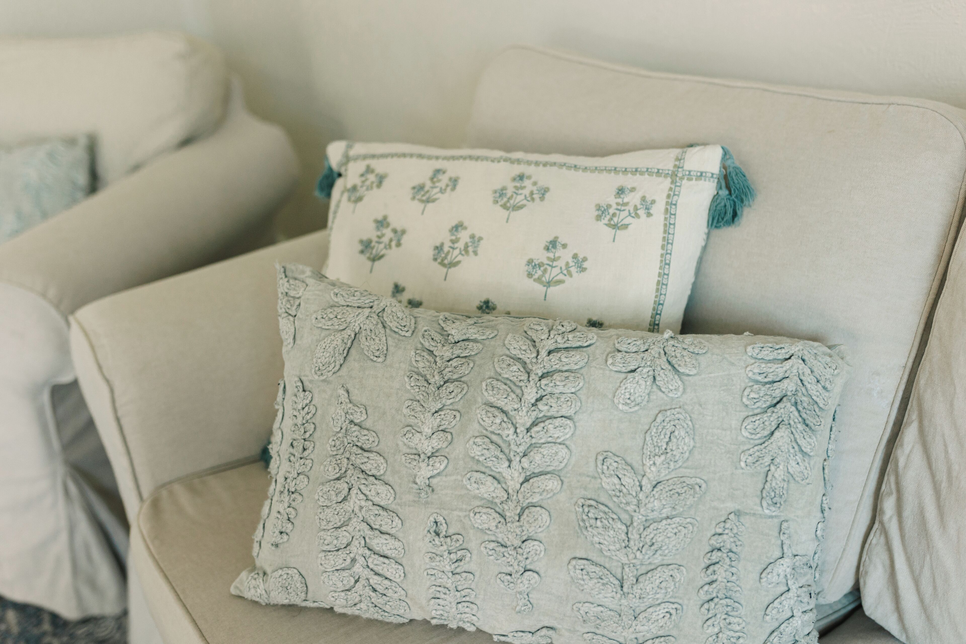 Um sofá bege com duas almofadas decorativas, uma estampada com flores e outra com folhagens.
