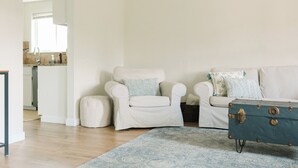 A living room with a white armchair, a blue patterned rug, and a vintage blue trunk.