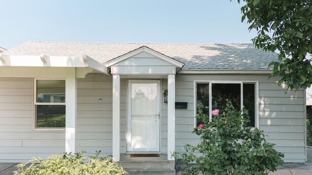 A single-story house with a front door, a small porch, and a window.
