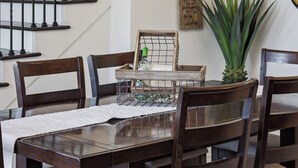 A dining area with a wooden table and chairs, a chandelier, a staircase, and a potted plant. - Relax, Play & Stay – Tropical Backyard Retreat + Game Room Near the Beach 🌊 (Indian Harbour Beach)