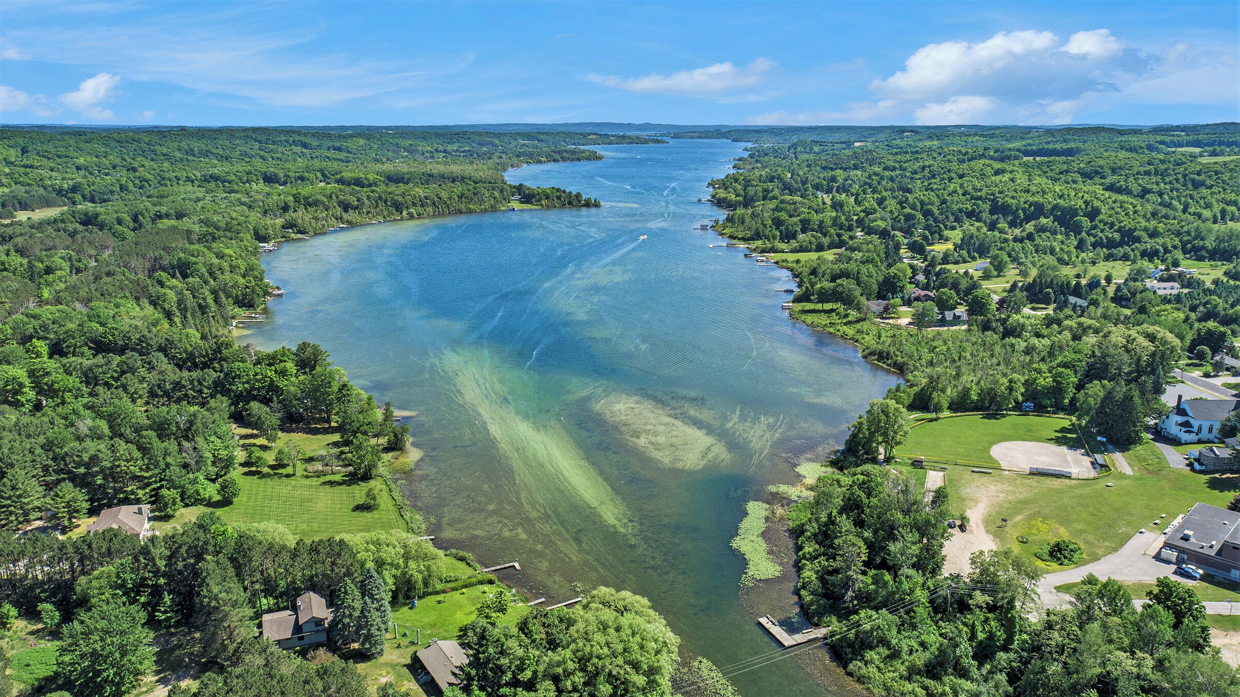 Vista aérea de un río rodeado de densos bosques y zonas residenciales con casas y un pequeño muelle.