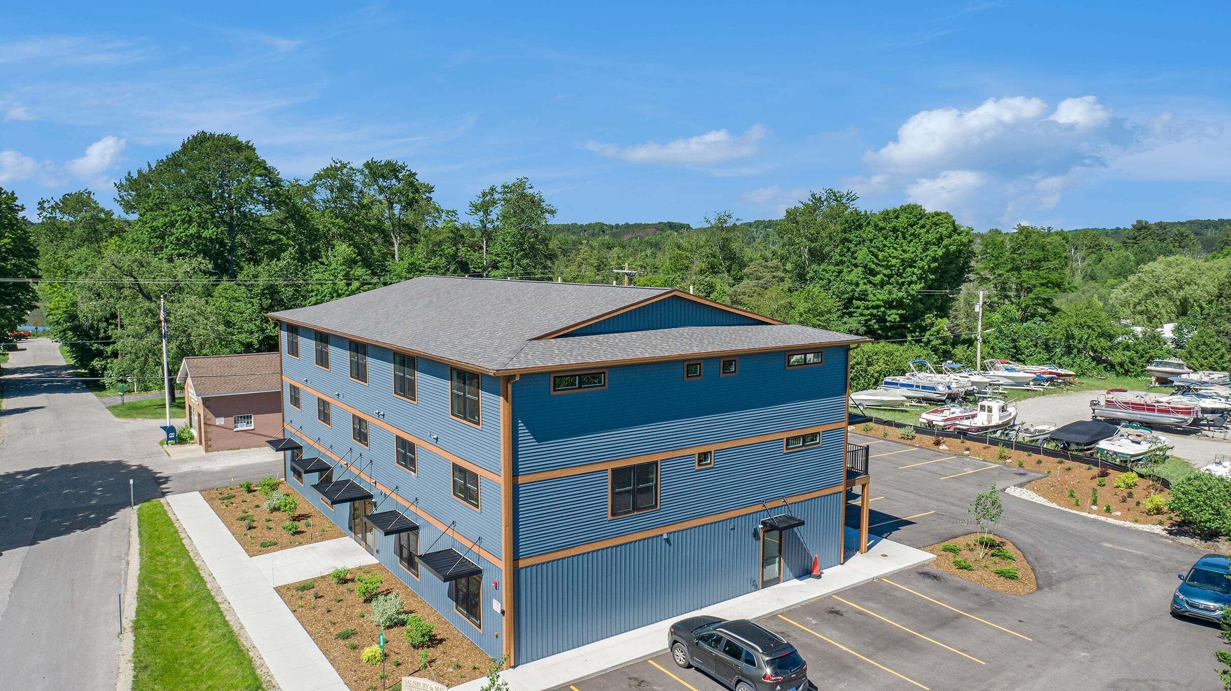 A two-story building with a blue exterior, a parking lot, and boats in the background.