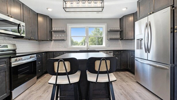 A modern kitchen with dark cabinetry, stainless steel appliances, and a central island with two chairs.