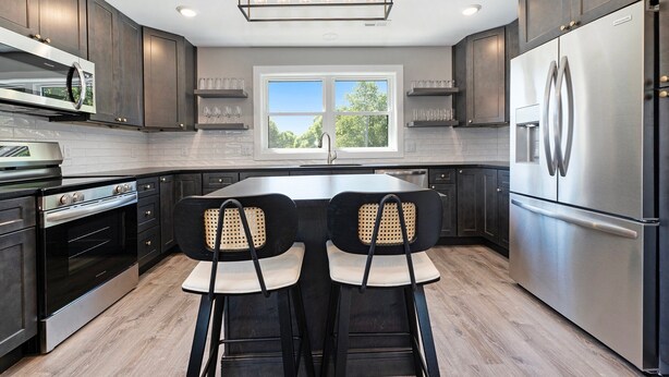 Una cocina moderna con armarios de madera oscura, electrodomésticos de acero inoxidable y un amplio ventanal que proporciona luz natural.