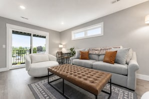 A living room with a sofa, armchair, and ottoman, a dining table with chairs, and a view through a sliding door.