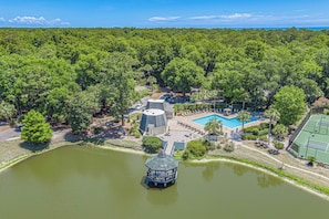 Vista aerea di un resort con piscina, campi da tennis e un padiglione su uno stagno.