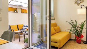 Una sala de estar moderna con un sofá amarillo, una puerta de vidrio que da a un balcón y una planta en maceta.