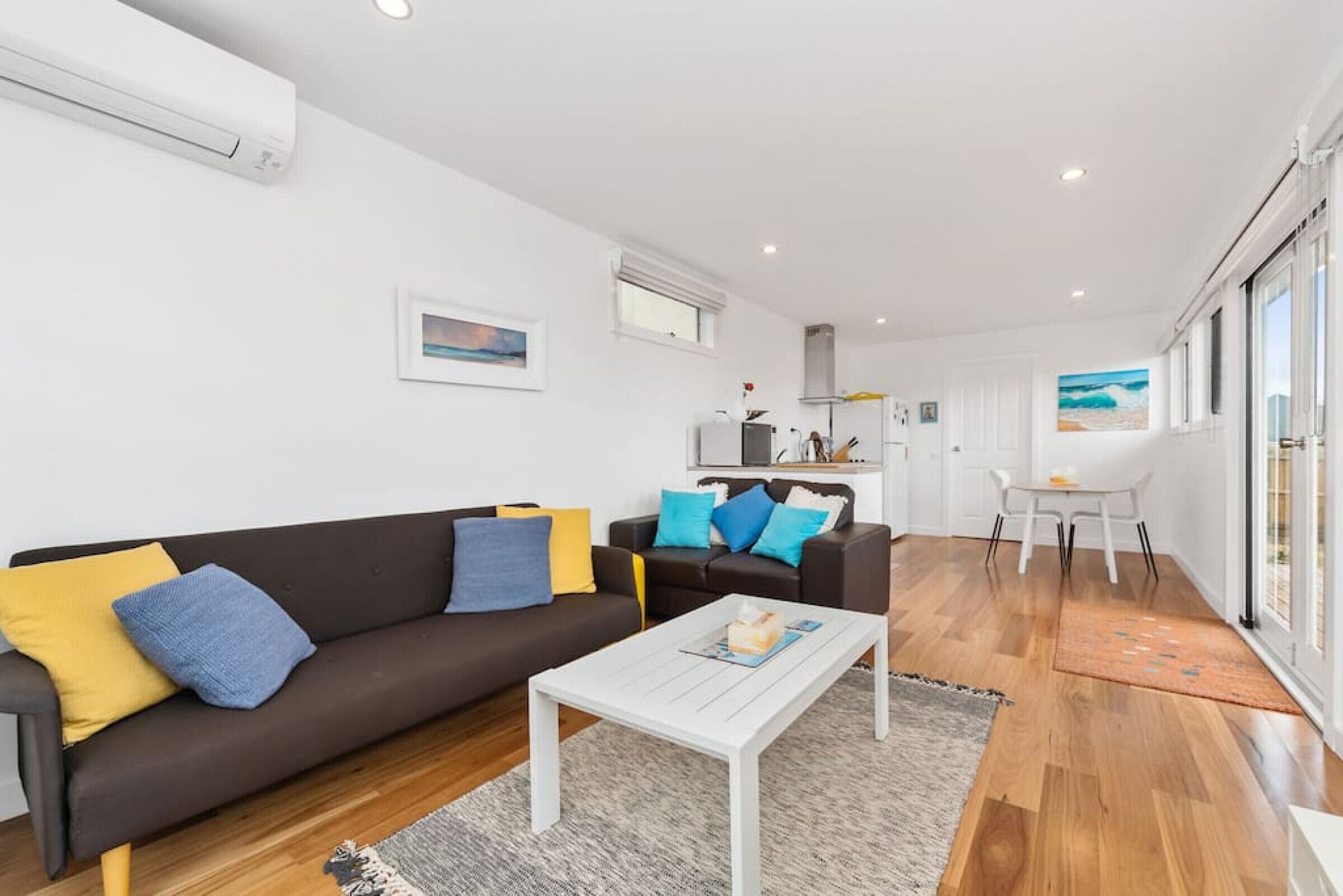 A modern living room with a brown sofa, white coffee table, and a dining area with a white table and chairs.