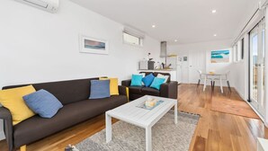 A modern living room with a brown sofa, white coffee table, and a dining area with a white table and chairs. - Quiet, luxurious Guest House - Couples Retreat (Mornington)
