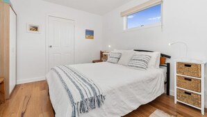 A bedroom with a bed, a window, a door, and a bedside table with baskets. - Quiet, luxurious Guest House - Couples Retreat (Mornington)