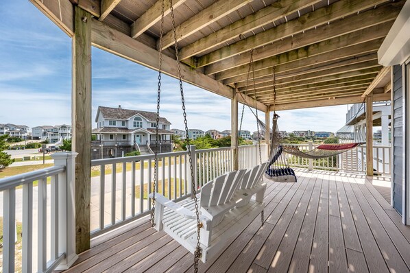 Une terrasse en bois avec une balançoire et un hamac, donnant sur un quartier résidentiel.