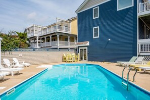 A swimming pool with lounge chairs and a two-story building with balconies.