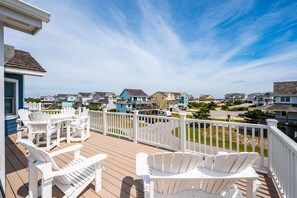 Une terrasse en bois avec des fauteuils Adirondack blancs, une clôture blanche et, en arrière-plan, une vue sur des maisons aux couleurs vives.