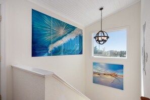 Una escalera con vistas al exterior, un cuadro abstracto de gran tamaño y un cuadro de paisaje más pequeño.