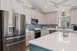 Une cuisine moderne dotée d’appareils électroménagers en acier inoxydable, de meubles de couleur claire, d’un grand îlot central et d’un ventilateur de plafond.