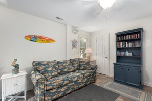 Una sala de estar con un sofá estampado, una estantería, un mueble bajo y un elemento decorativo en la pared.