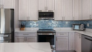 A modern kitchen with light-colored cabinets, a stainless steel refrigerator, a built-in oven, a microwave, and a toaster. - Waves of Joy: Oceanside, Private Heated Pool, Hot Tub (Nags Head)