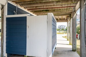 Ein überdachter Außenbereich mit einem blau-weißen Gebäude, Holzbalken und einem sichtbaren Weg, der zu einem Wohngebiet führt.