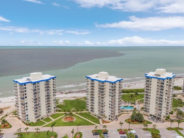 A high-rise hotel with multiple floors, a central courtyard, and a beach view. - Steps to the Beach, Heated Pool, Tennis, Shuffleboard - FMB - Condo Seaside Sanctuary - Roelens (Fort Myers Beach)