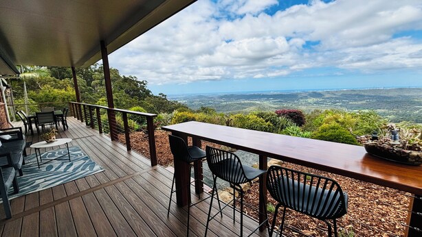 Una terraza de madera con mobiliario exterior, una mesa y sillas, con vistas a un paisaje pintoresco.